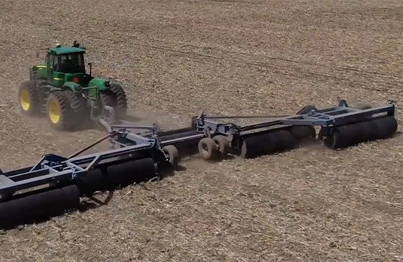 Powerful tractor paired with Brandt land roller, flattening rough terrain for improved planting conditions.