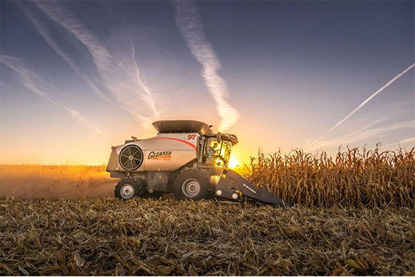 Gleaner S97 combine harvesting corn at sunset with a dramatic sky and contrails in the background.