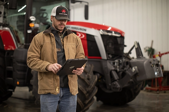 Farmer reading news on an iPad while standing next to his Massey Ferguson tractor from AgRevolution.